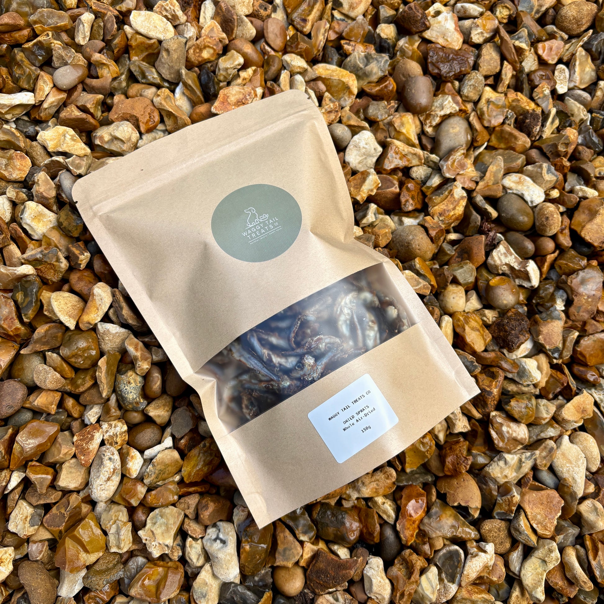 Kraft paper bag with a green label on a gravel background showing sprats a natural dog treat