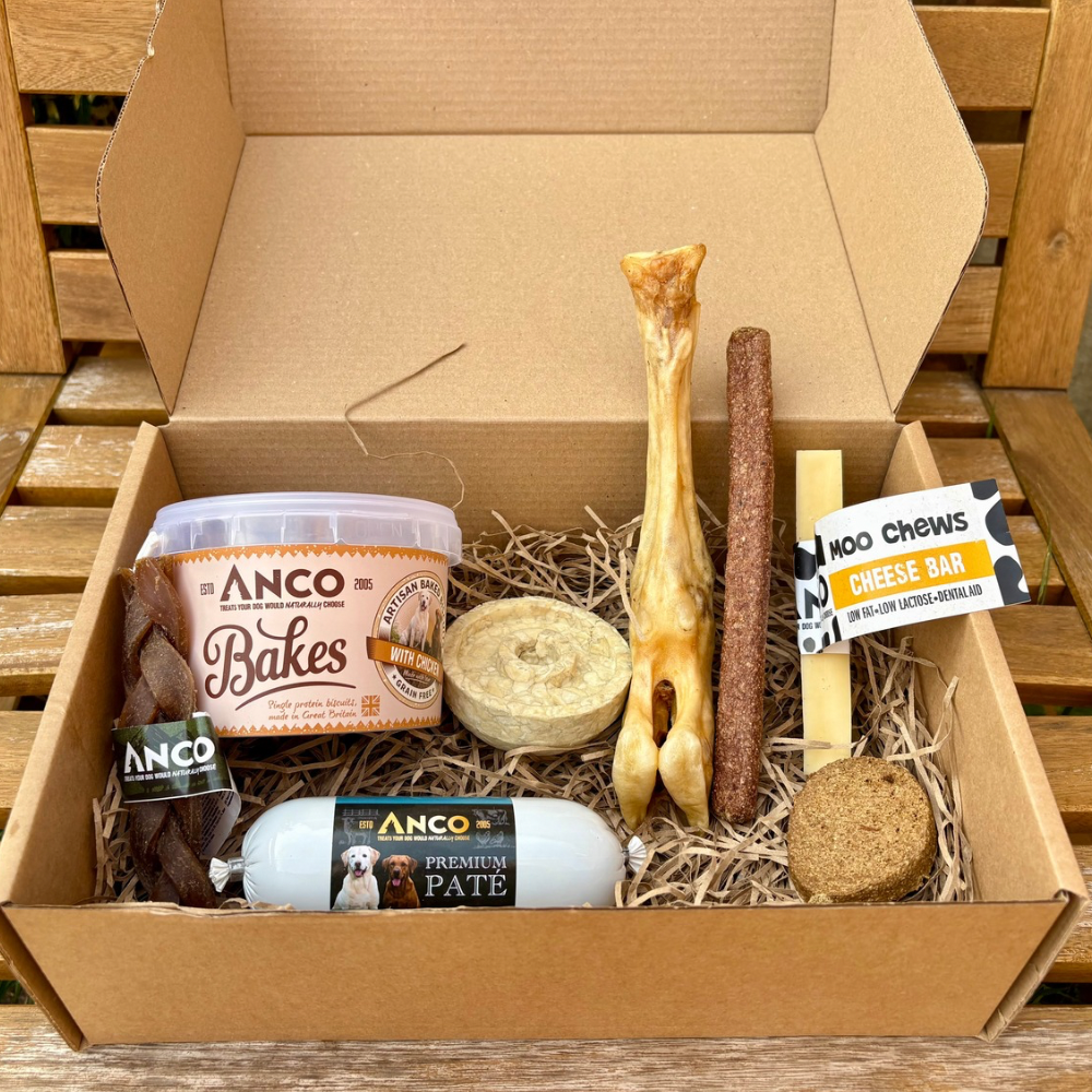 Dog treat and toy box with various dog treats including Anco Bakes and Moo Chews on a wooden surface.
