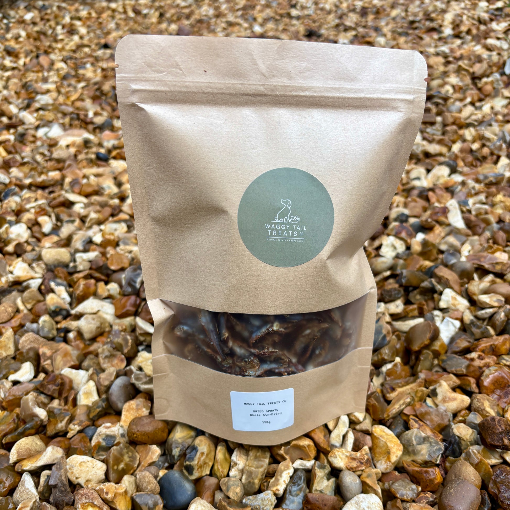 Kraft paper bag with a green label on a gravel background showing sprats a natural dog treat