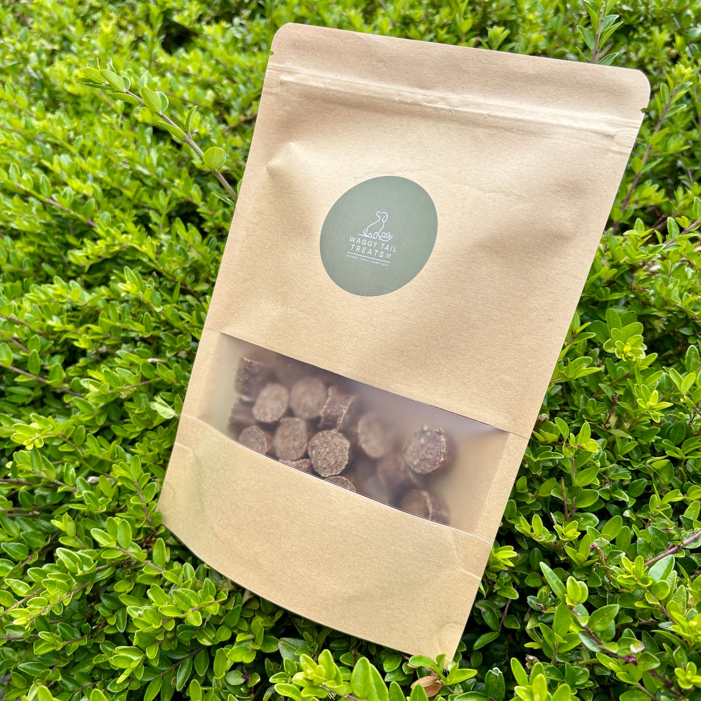 Kraft paper packaging with a clear window showing dark-colored items on a green leafy background