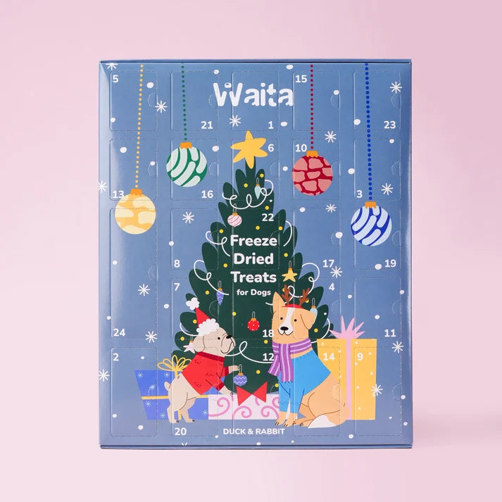 A blue Christmas advent calendar for dog freeze-dried treats by Duck & Rabbit, featuring illustrated dogs, a decorated tree, ornaments, and gift boxes on a light pink background.