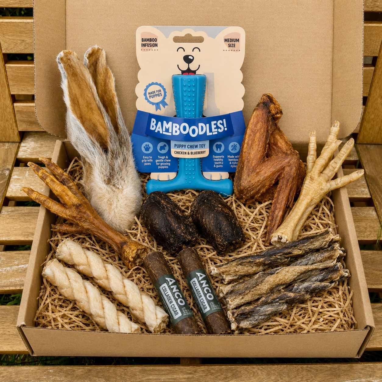 Assorted dog chew toys including Bamboodles! in a cardboard box on a wooden pallet.